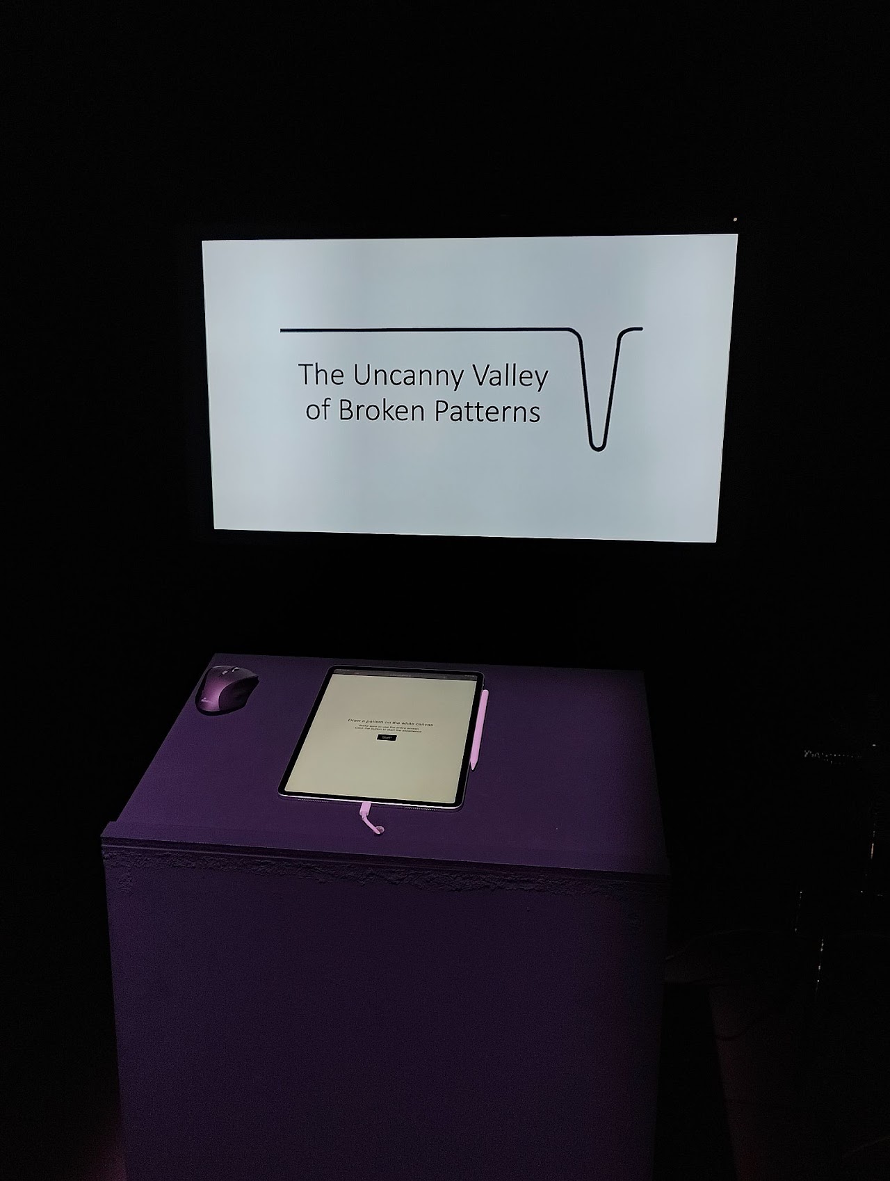 Full exhibition setup with the projected title screen above an interactive tablet on a purple podium