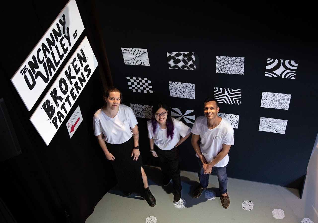 The three team members posing in front of the exhibit's pattern display wall